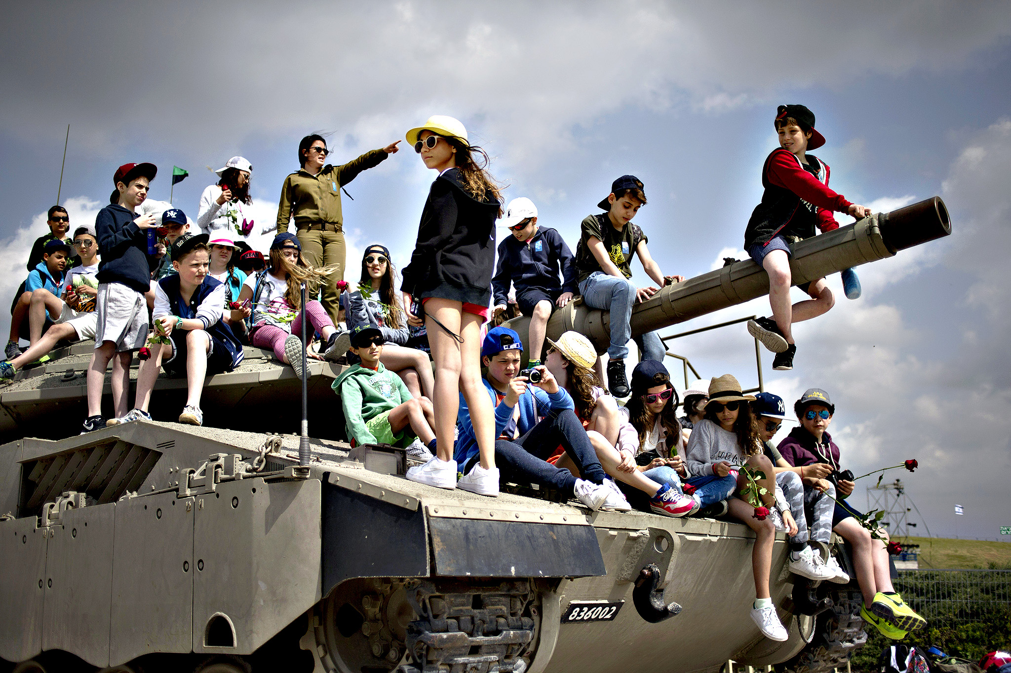 School children from Belgium sit on a tank on display as they listen to an Israeli soldier speaks about Israel's wars, near the wall of names of fallen soldiers, at the Armored Corps memorial, before a ceremony marking the annual Memorial Day for soldiers and civilians killed in more than a century of conflict between Jews and Arabs, in Latrun near Jerusalem, Israel, Wednesday, April 22, 2015. Israel came to a standstill on Wednesday as sirens wailed across the country on its annual Memorial Day for fallen soldiers and victims of terrorism.